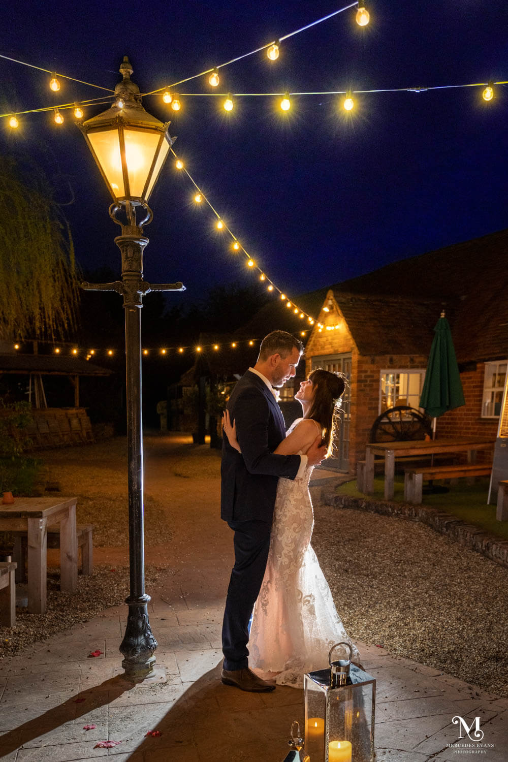 the bride and groom embrace under the lamp stand and festoon lights in the courtyard at Cantley House hotel