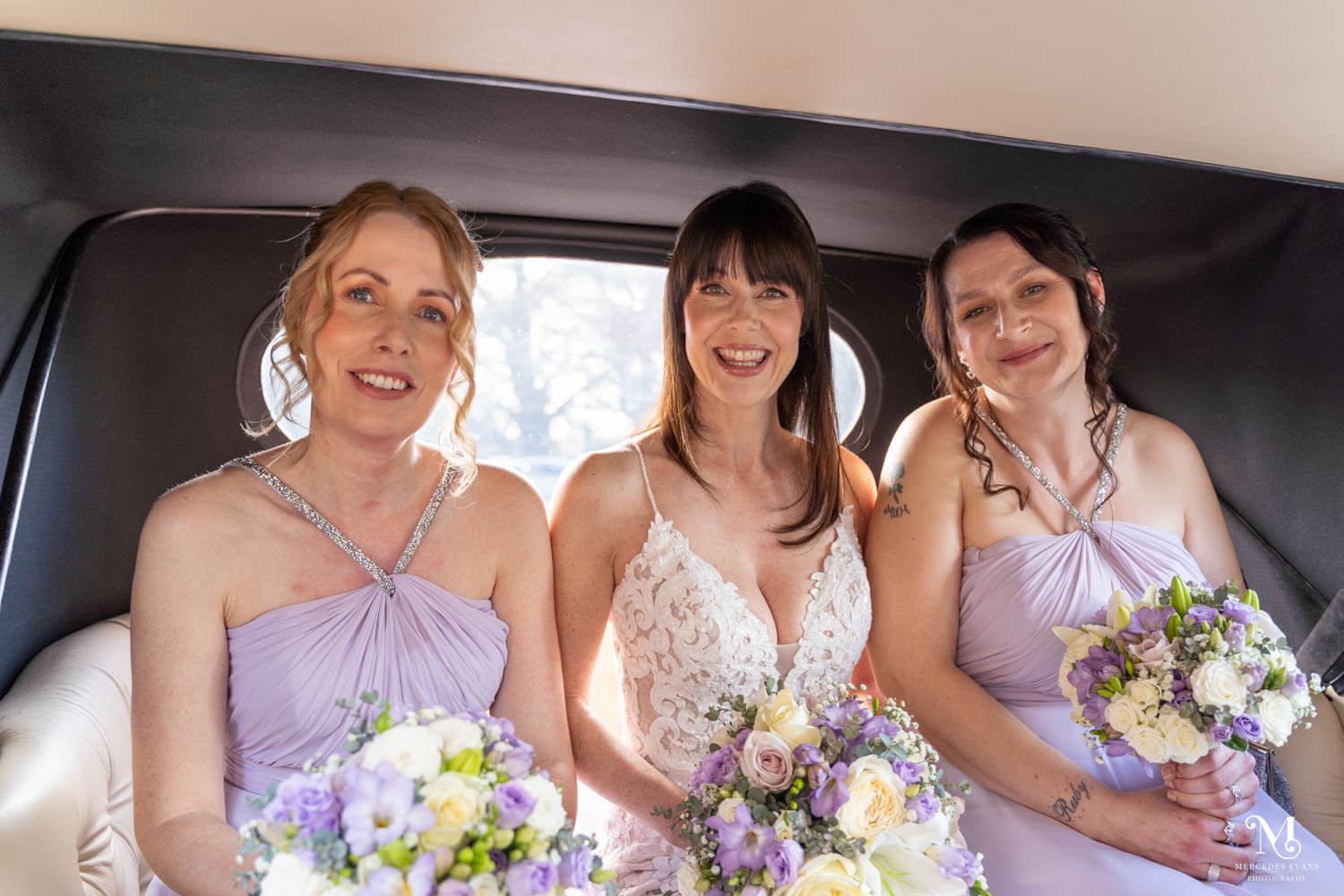 The bride and her bridesmaids sit smiling in the vintage wedding car