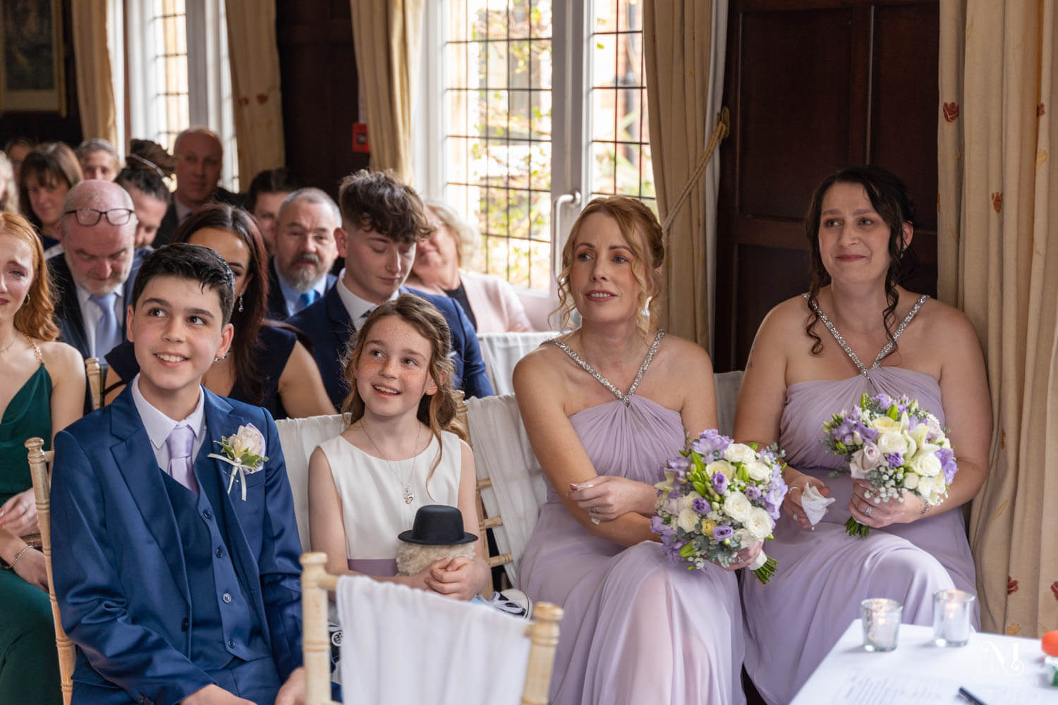 the children of the couple and the adult bridesmaids sit and watch the couple getting married