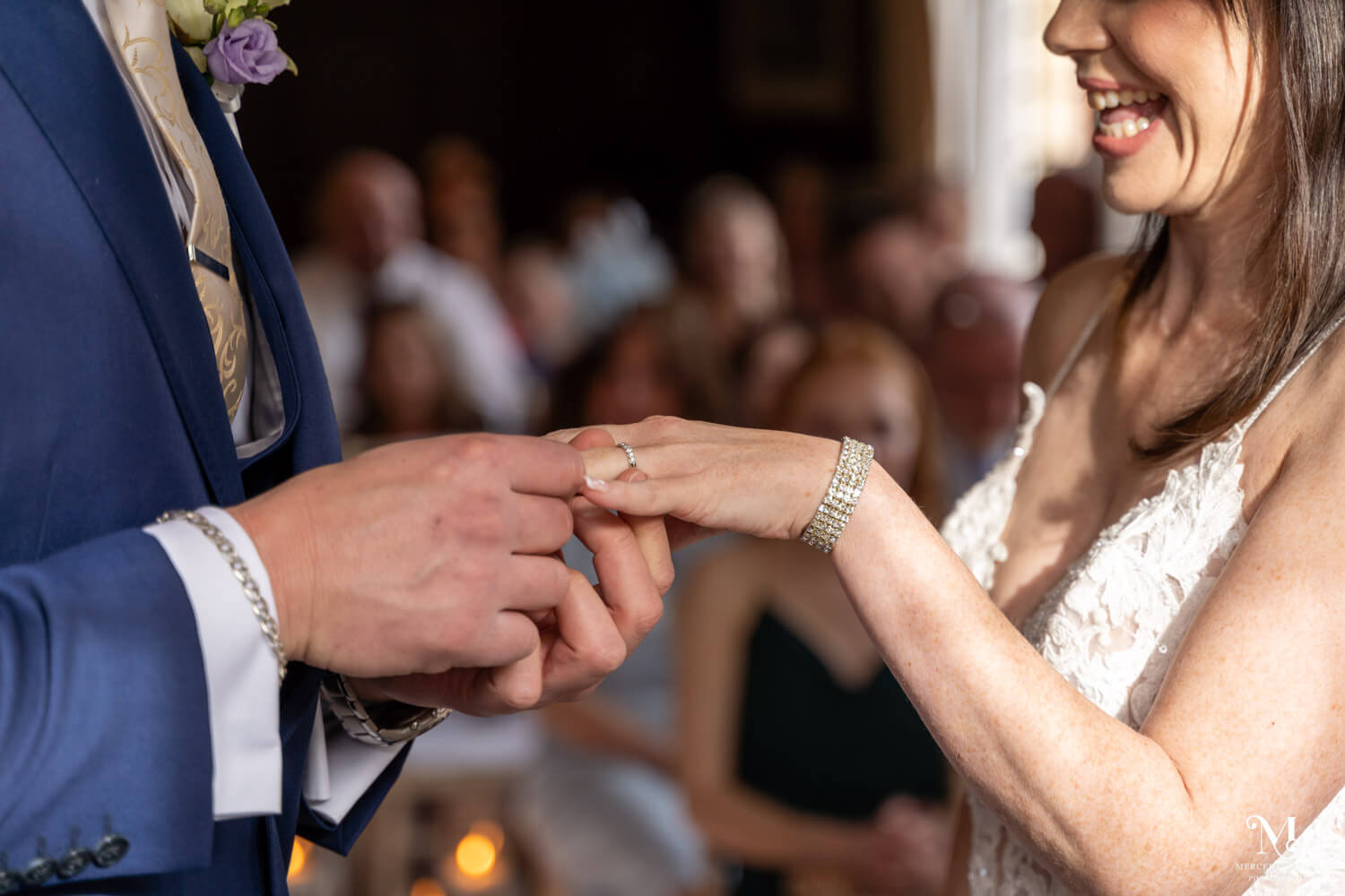 the groom puts the bride's wedding ring on her finger during their wedding ceremony in the Oak room at Cantley House Hotel