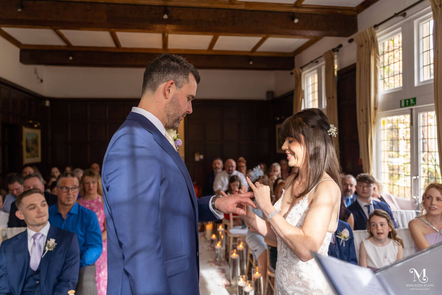 the bride puts the groom's wedding ring on his finger during their wedding ceremony in the Oak room at Cantley House Hotel