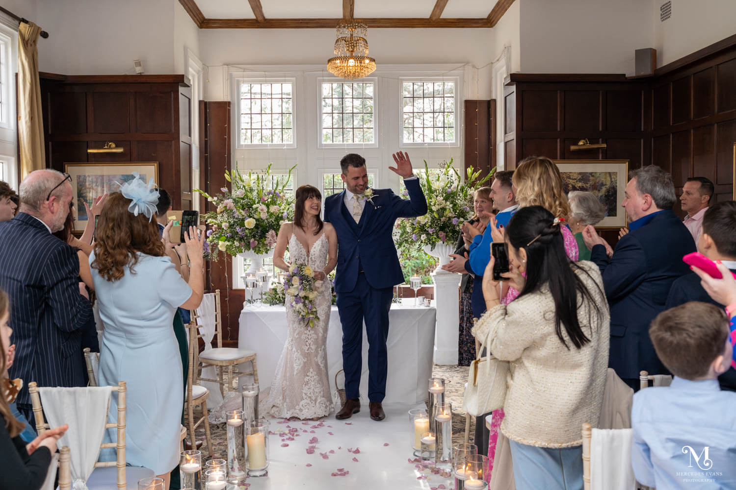 the bride and groom smile at guests and wave as they leave the ceremony in the Oak room at Cantley House Hotel