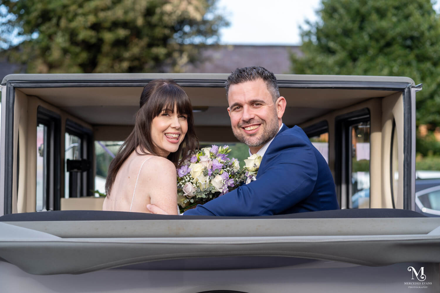 the bride and groom sit together and look back over their shoulders as they sit in their vintage wedding car