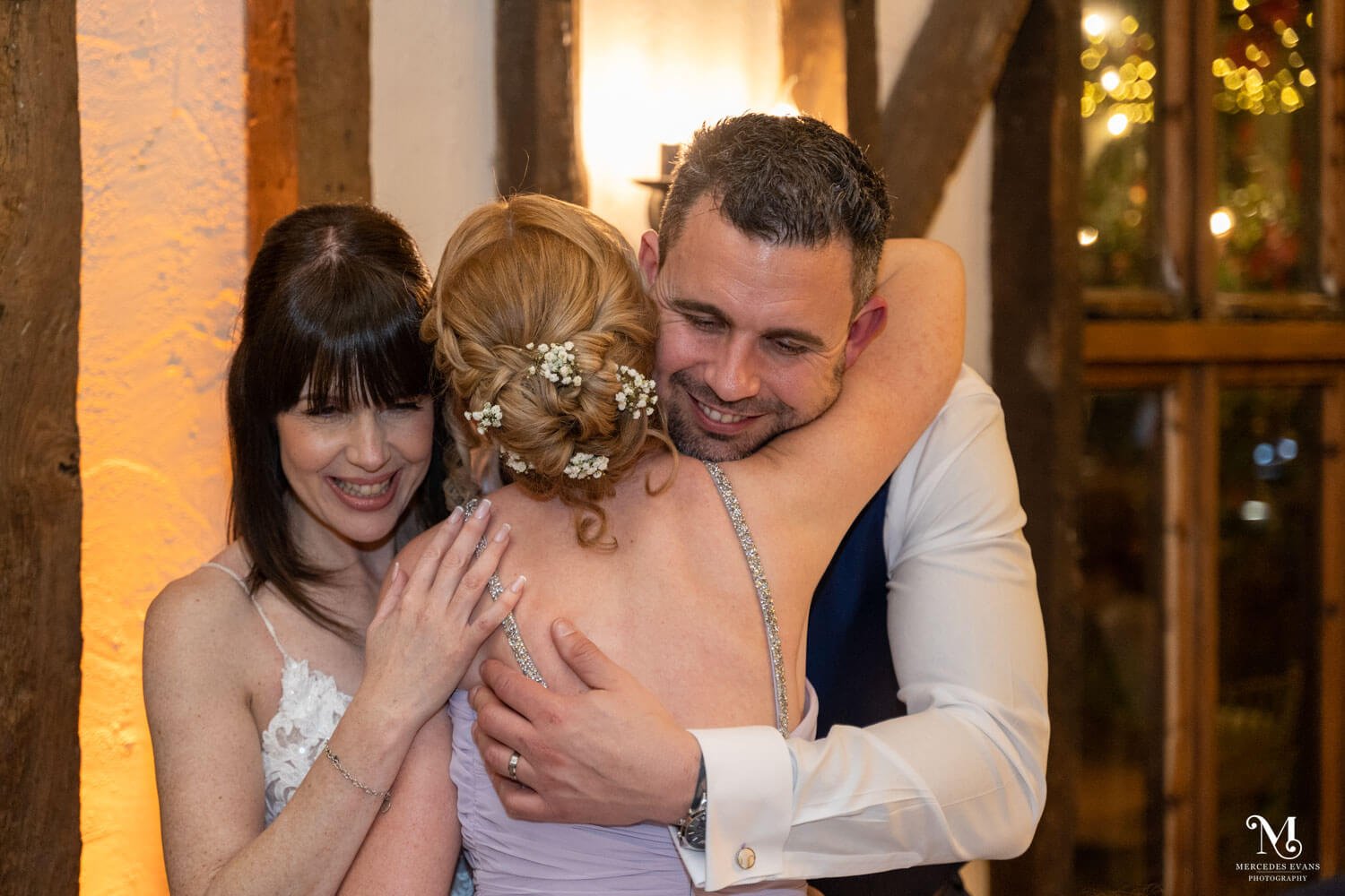 the bride and groom both hug the maid of honour during the evening reception