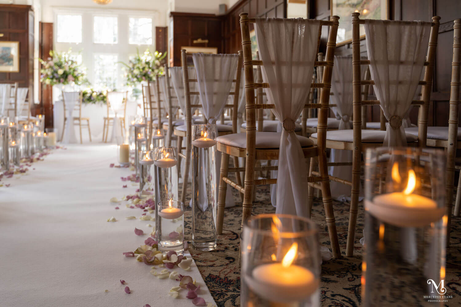 a view down the aisle of the chiavari chairs, vases with floating candles and lilac and white petals