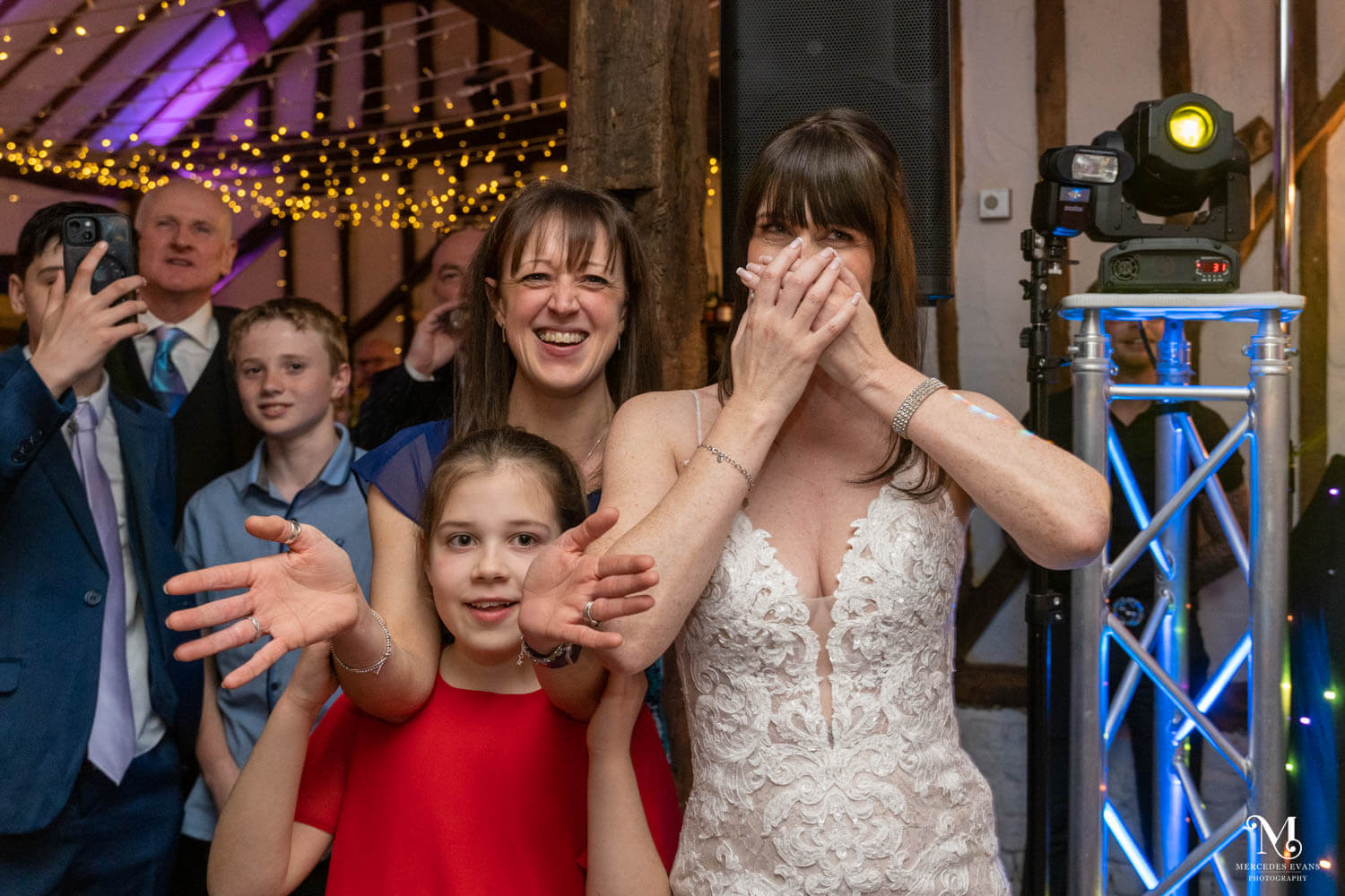 the bride puts her hands over her face and friends laugh and clap as they watch the dance routine
