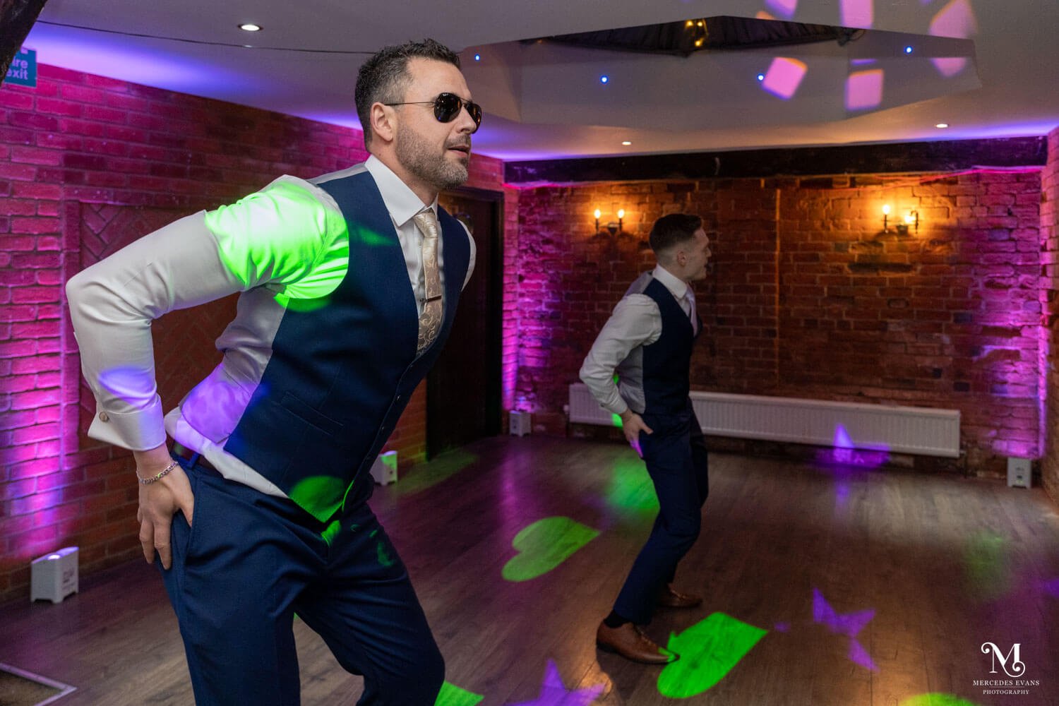 the groom and groomsmen do a co-ordinated dance on the dance floor with green and violet lights