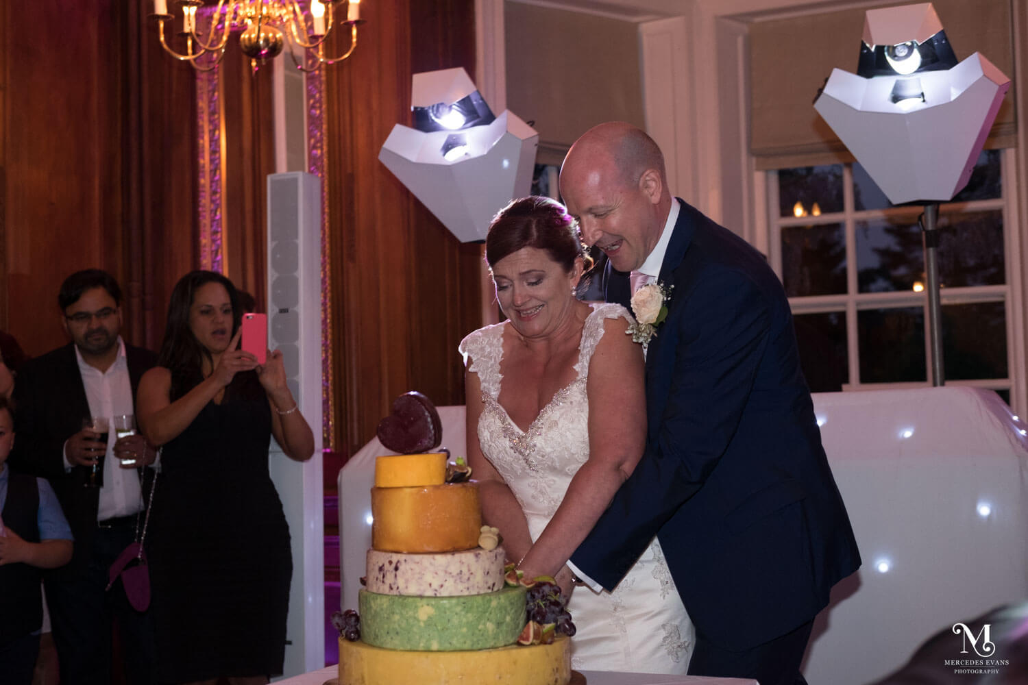 the bride and groom try to cut the cheese tower, watched by guests