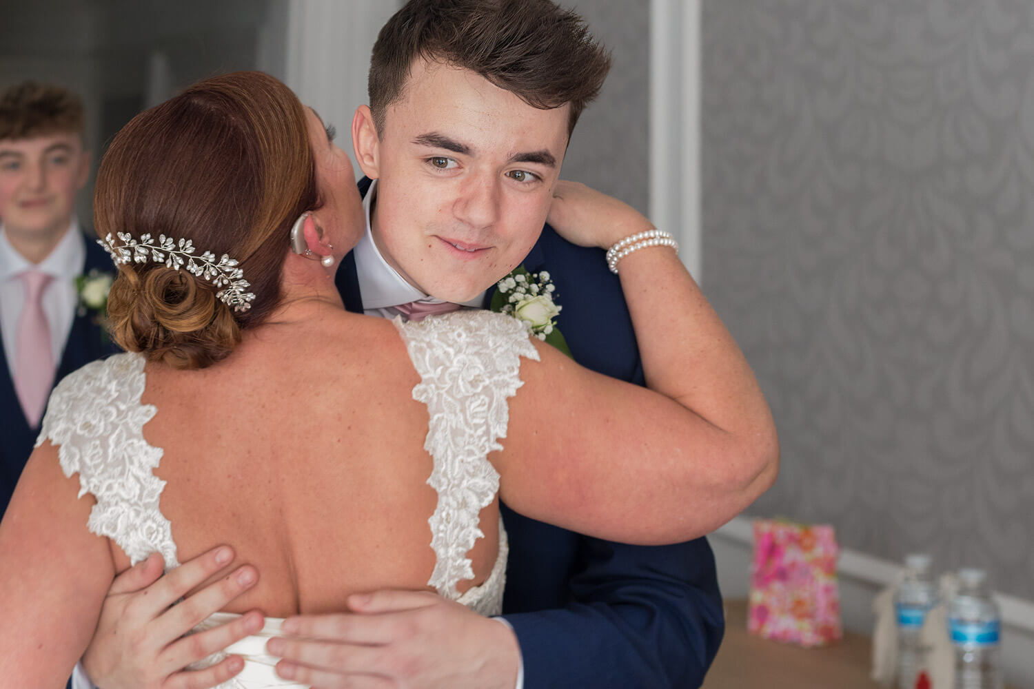 smiling young man is kissed by his mum, the bride, his brother stand sbehind him