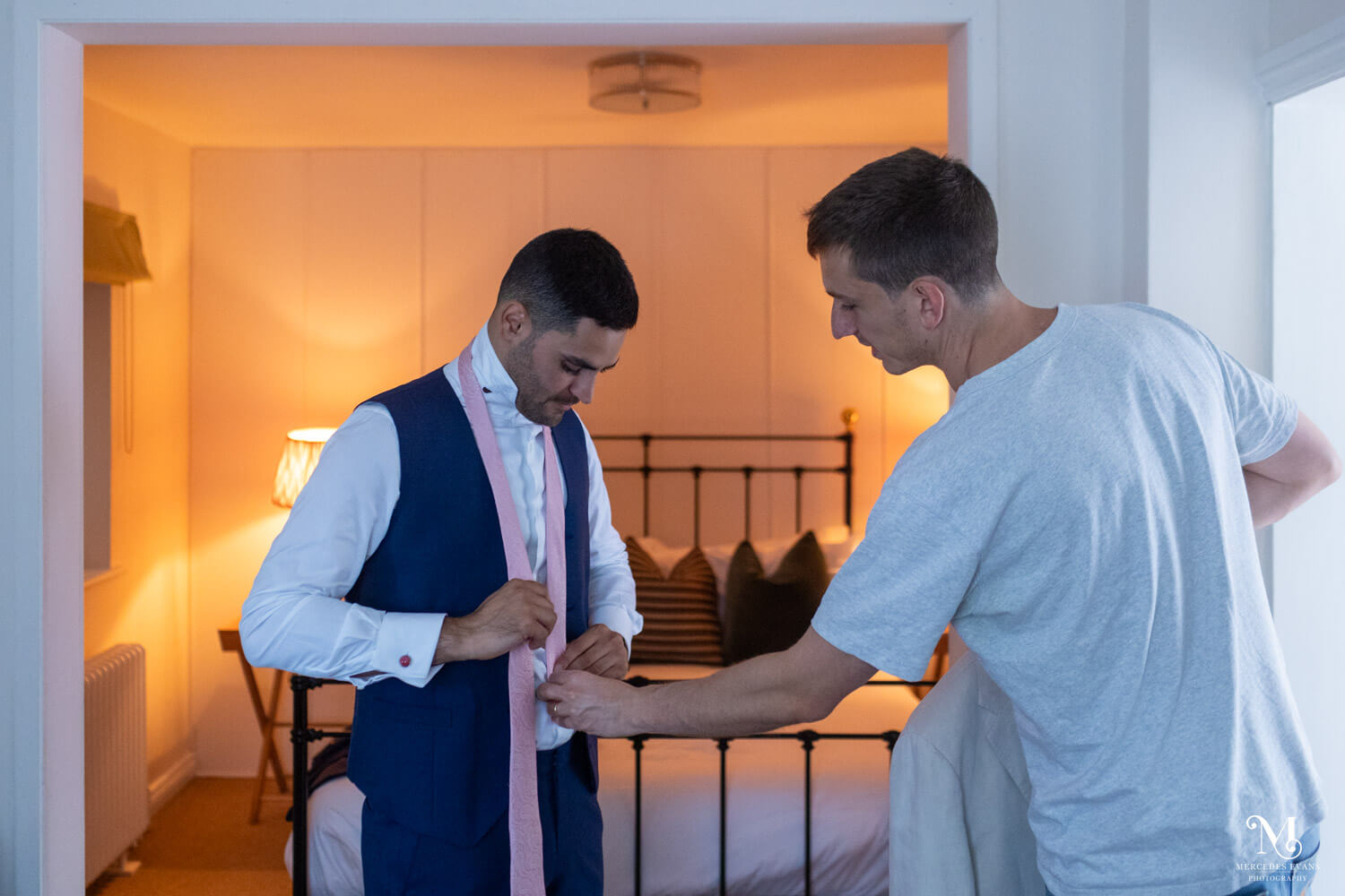 a groomsman alters the groom's tie length as they get ready in the lodge at Millbridge court