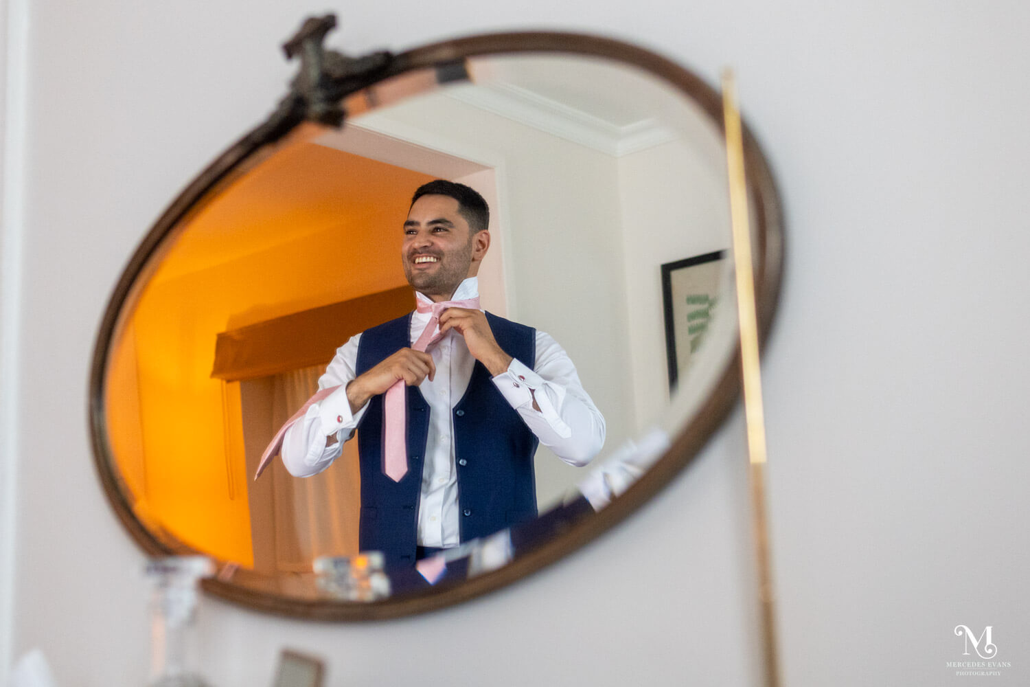 a mirror reflection of the smiling groom doing up his pink tie