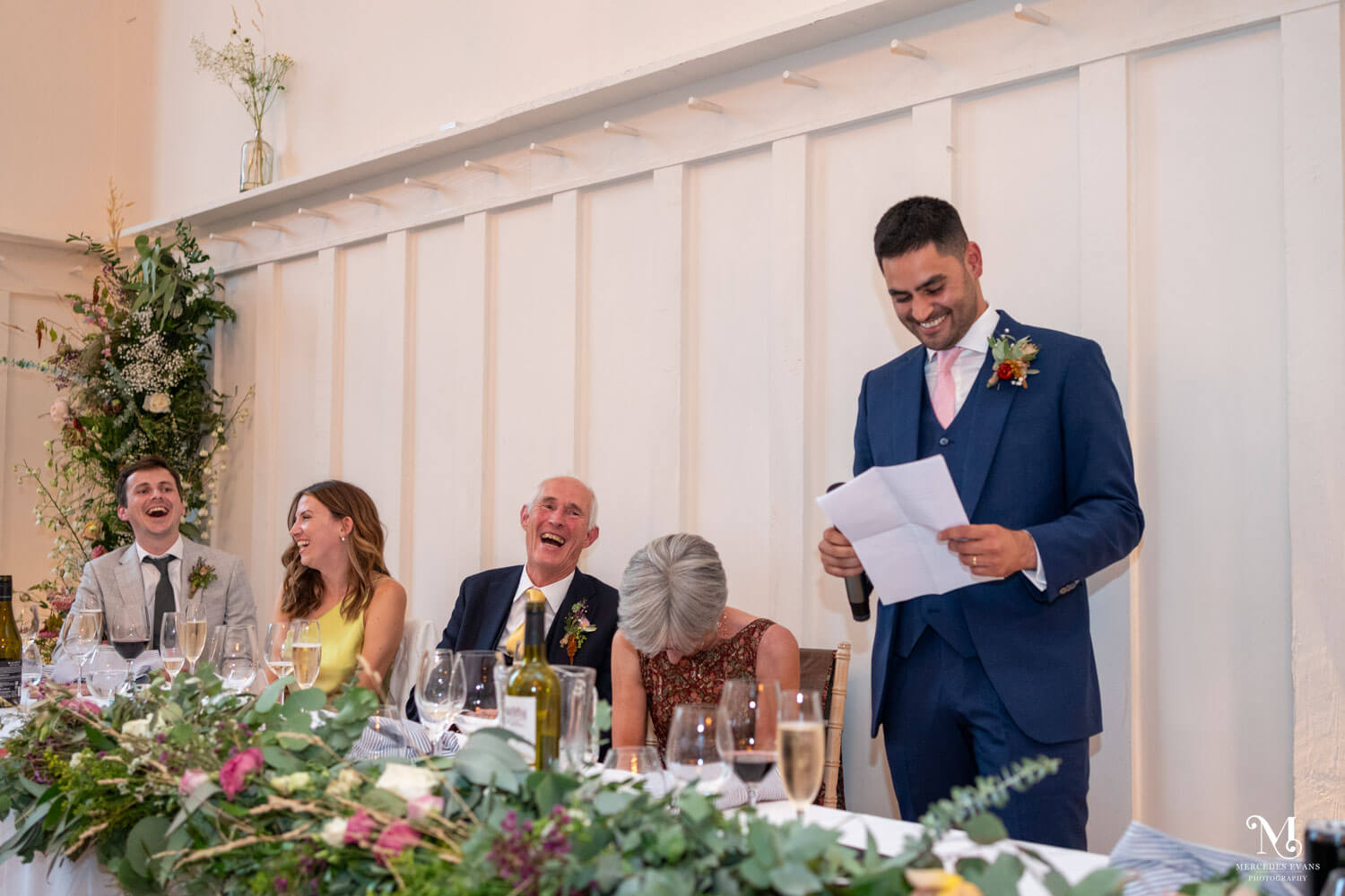 the groom stands making his speech, all around him are howling with laughter