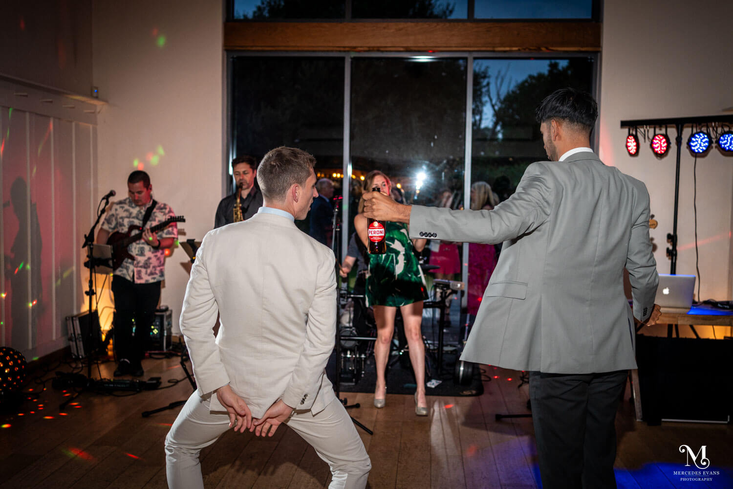 two men dance together, with the wedding band behind them