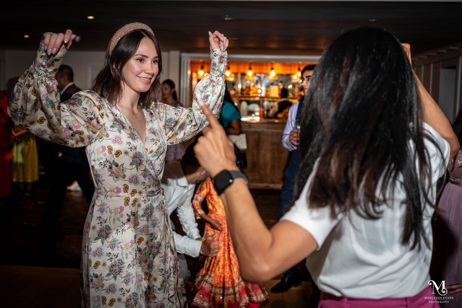 two women dance with arms in the air during the evening reception, the bar at millbridge court is in the background