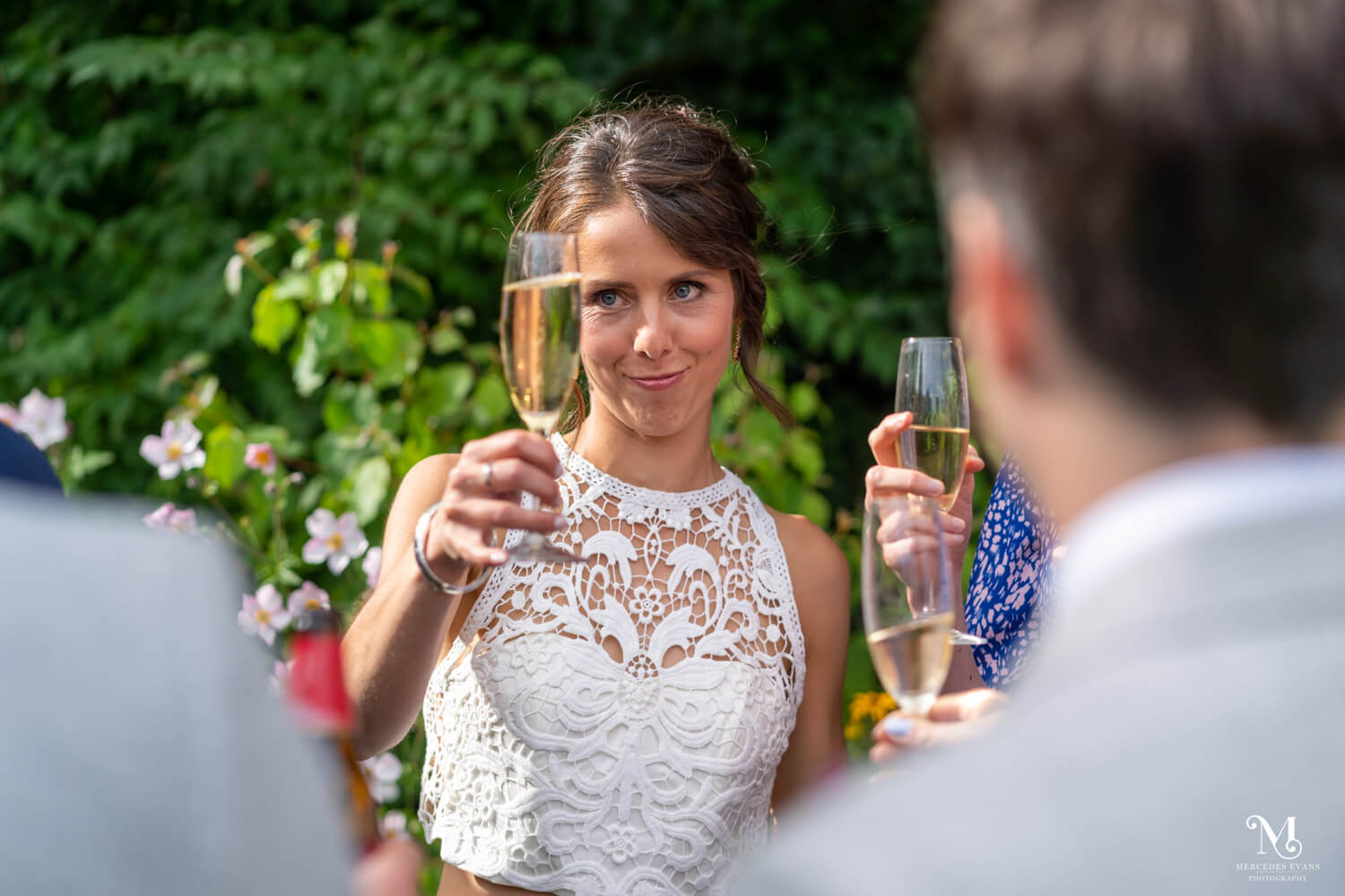 the bride wearing a white lace top, shares a champagne toast with guests
