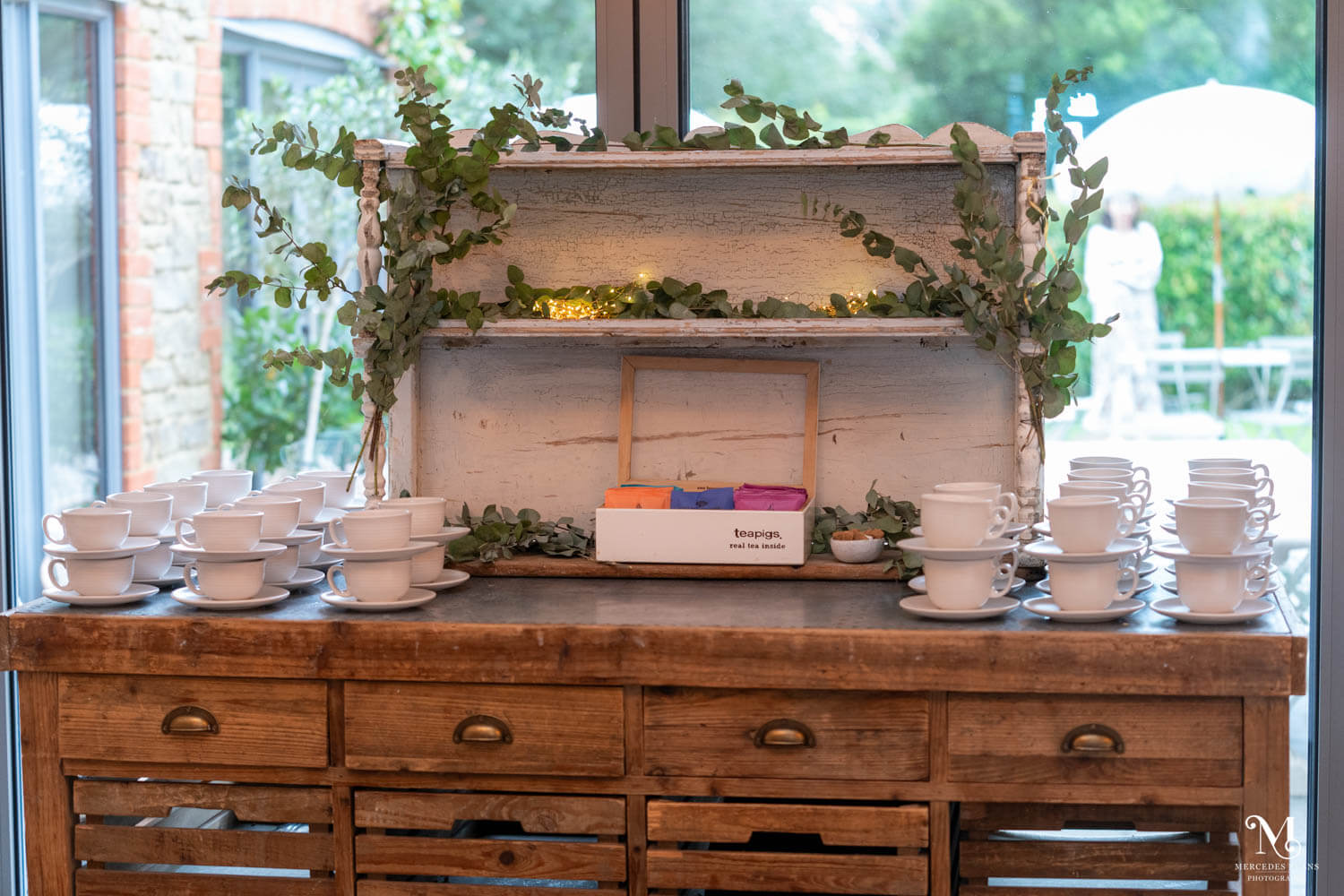 an old oak dresser serves as tea and coffee station, it's decorated with eucalyptus leaves and twinkling fairy lights