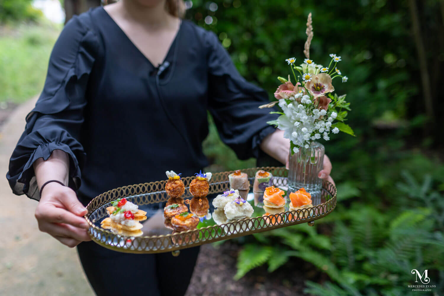 canapés carried on a reflective tray with a small vase of flowers