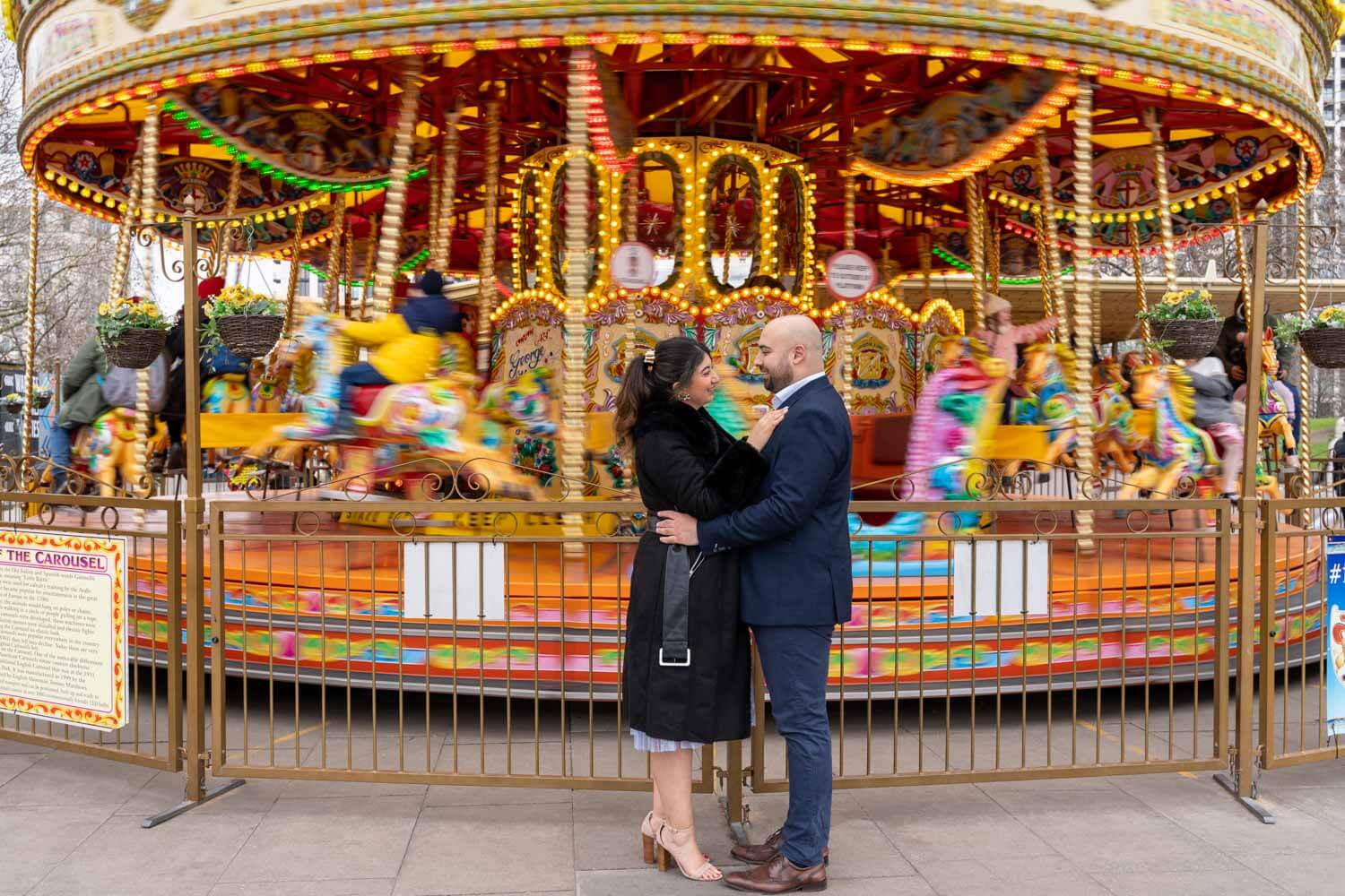 couple embrace in front of a moving fairground carousel