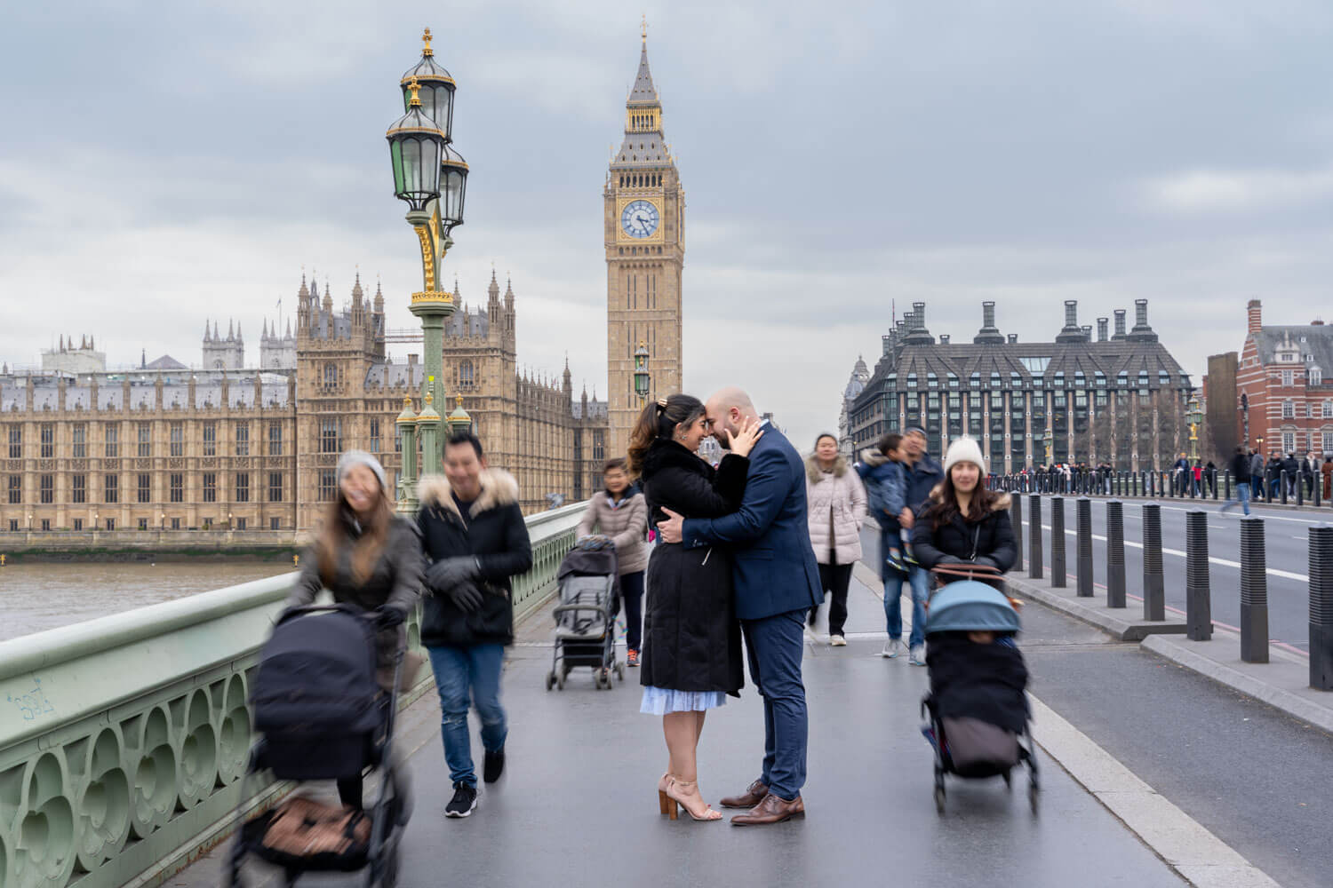 couple stand facing each other and embrace as pedestrians walk past on westminster bridge
