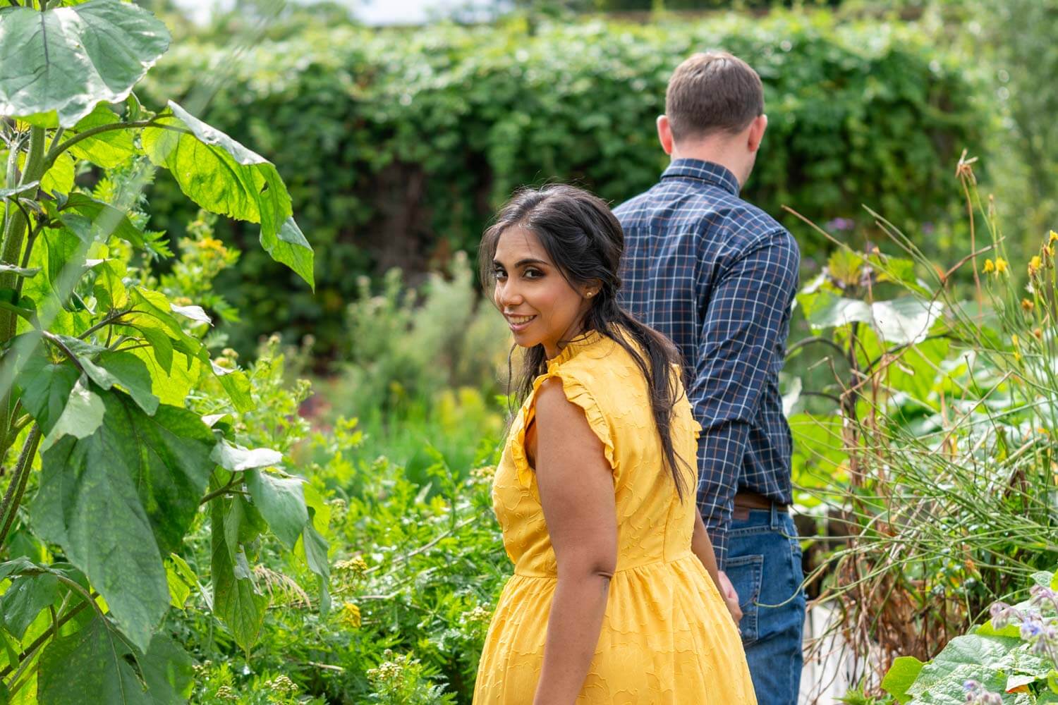 man leads his fiancée, through a garden, she looks back