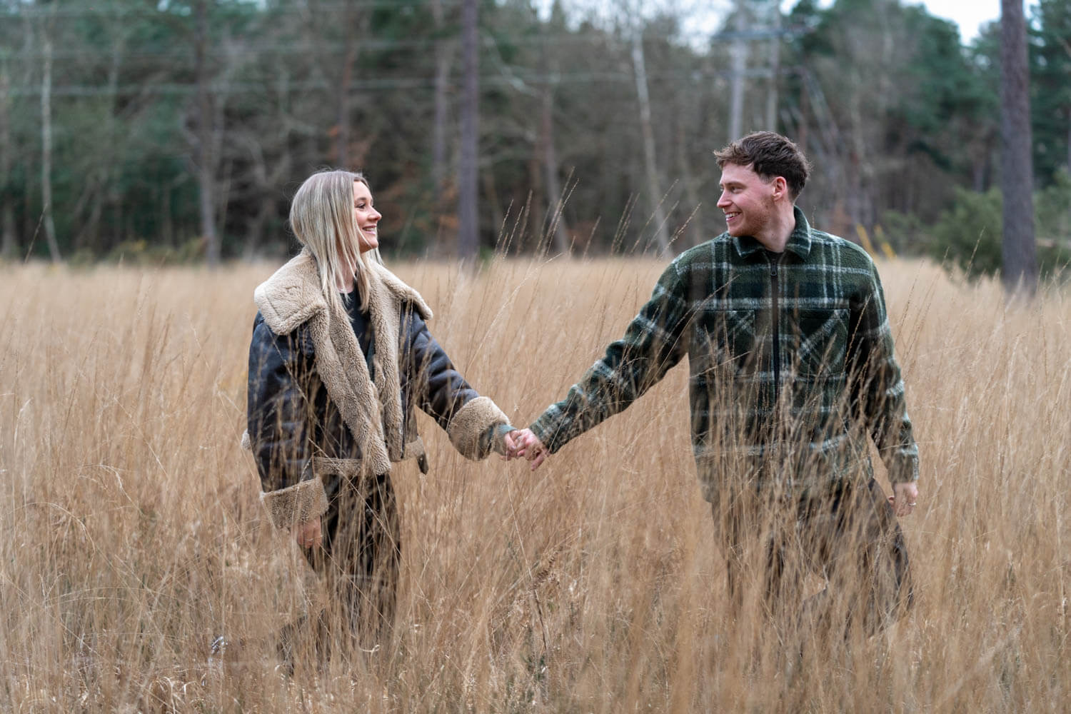 young couple walk hand in hand in the very long golden grass