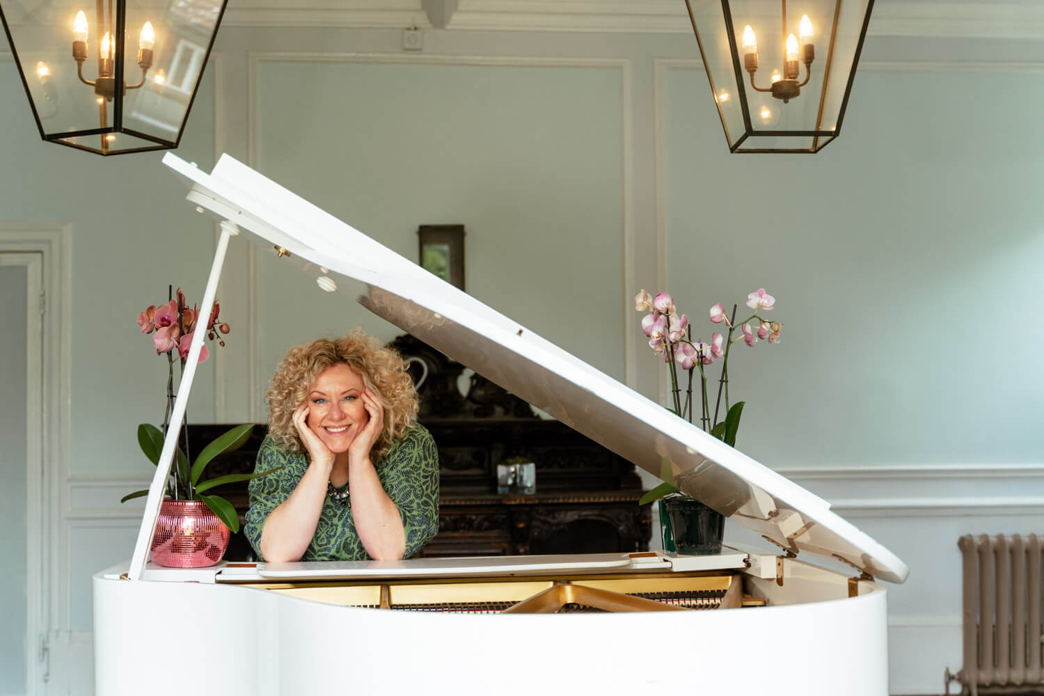 female pianist leans on her hands, with her elbows on a white grand piano