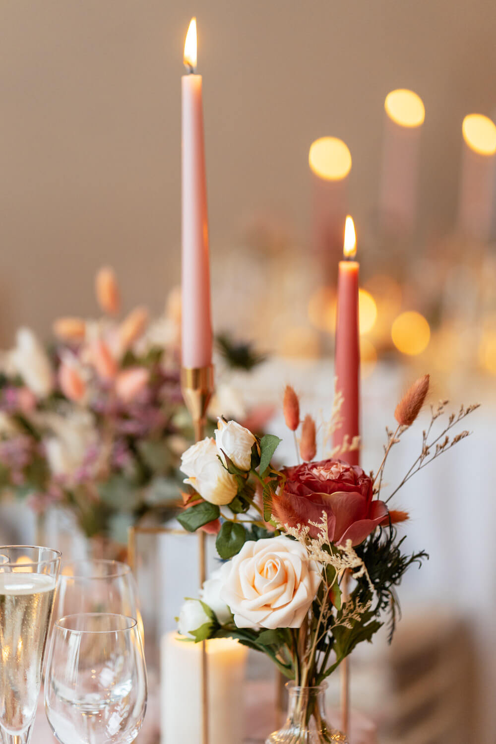 pale pink taper candles with glass vases of dark and pale pink roses, grasses and bunny tails decorate the wedding breakfast tables