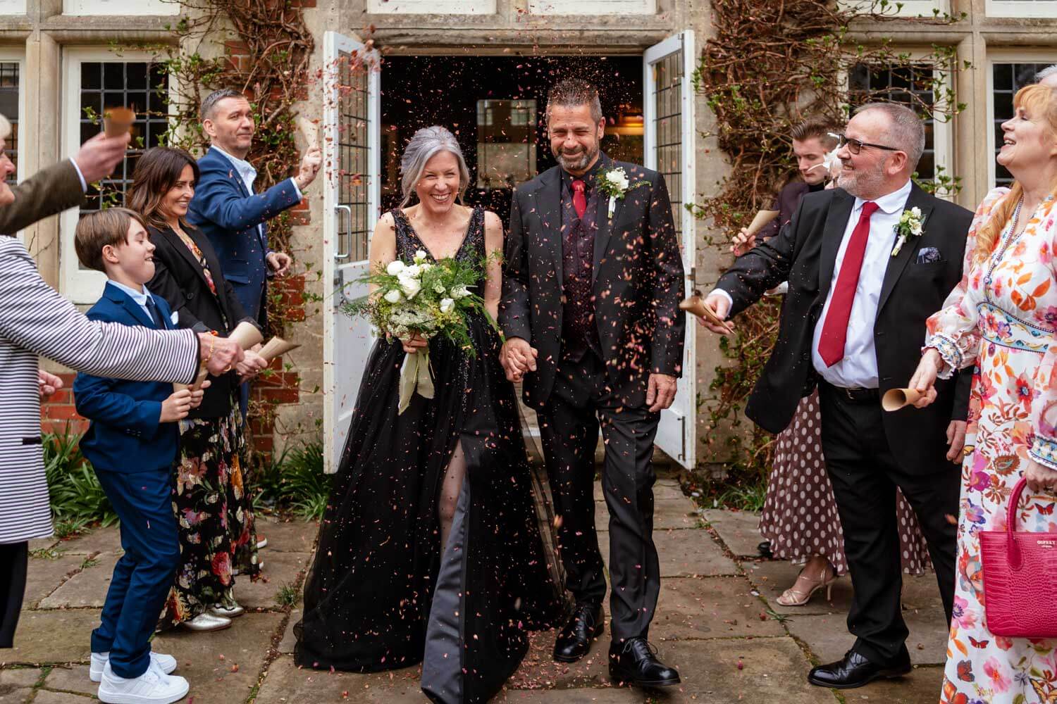 the laughing bride and groom are welcomed with clouds of dried petal confetti as they exit the doors of the Oak Room at Cantley House