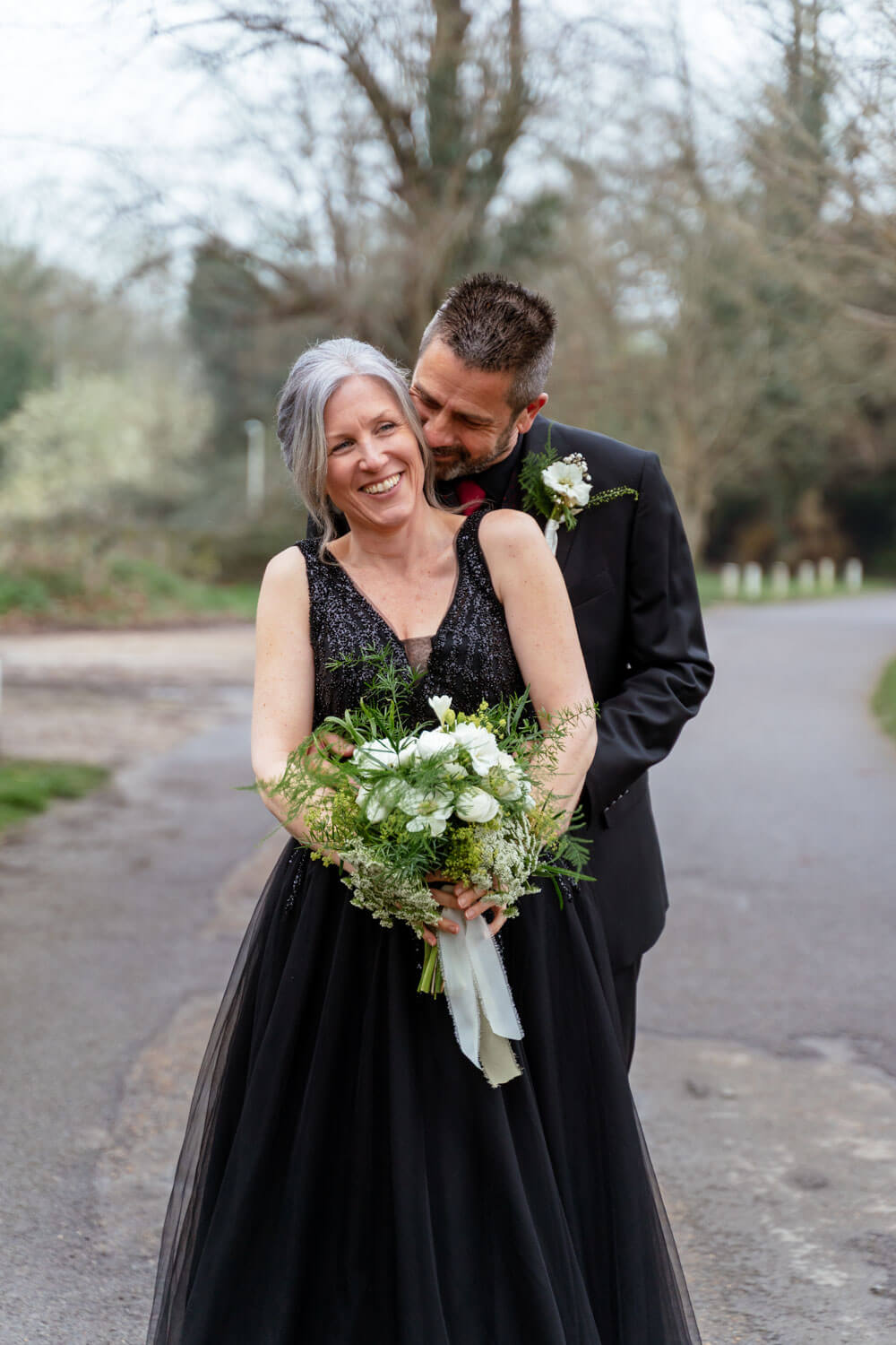 the groom stands behind the laughing bride and whispers into her ear as he holds her waist