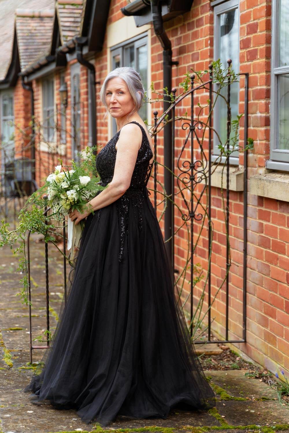 the beautiful bride wears a long black dress and carries a white and green bouquet