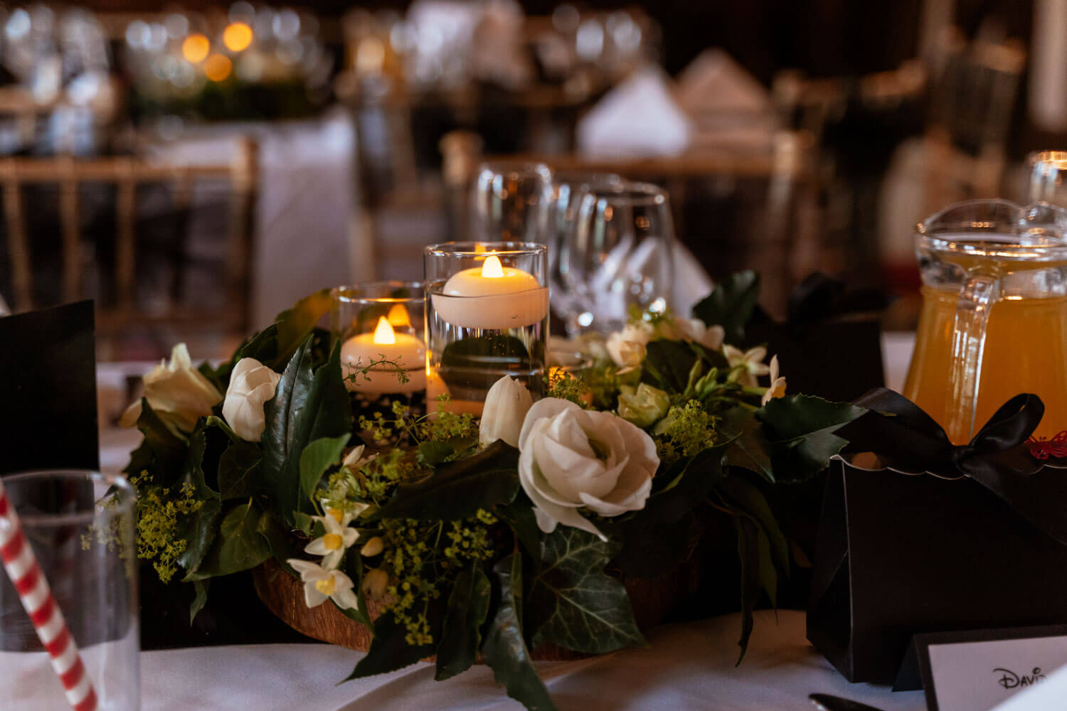 black themed wedding breakfast detail of cream roses, pale daffodils, ivy and alchemilla mollis, with 3 glass vases and floating tea lights
