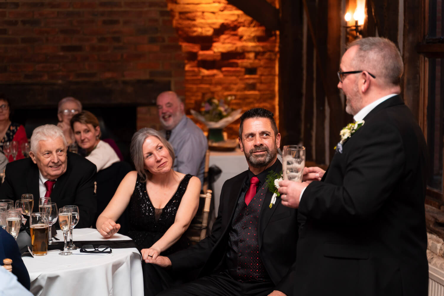the bride and groom smile at the best man as he makes his speech