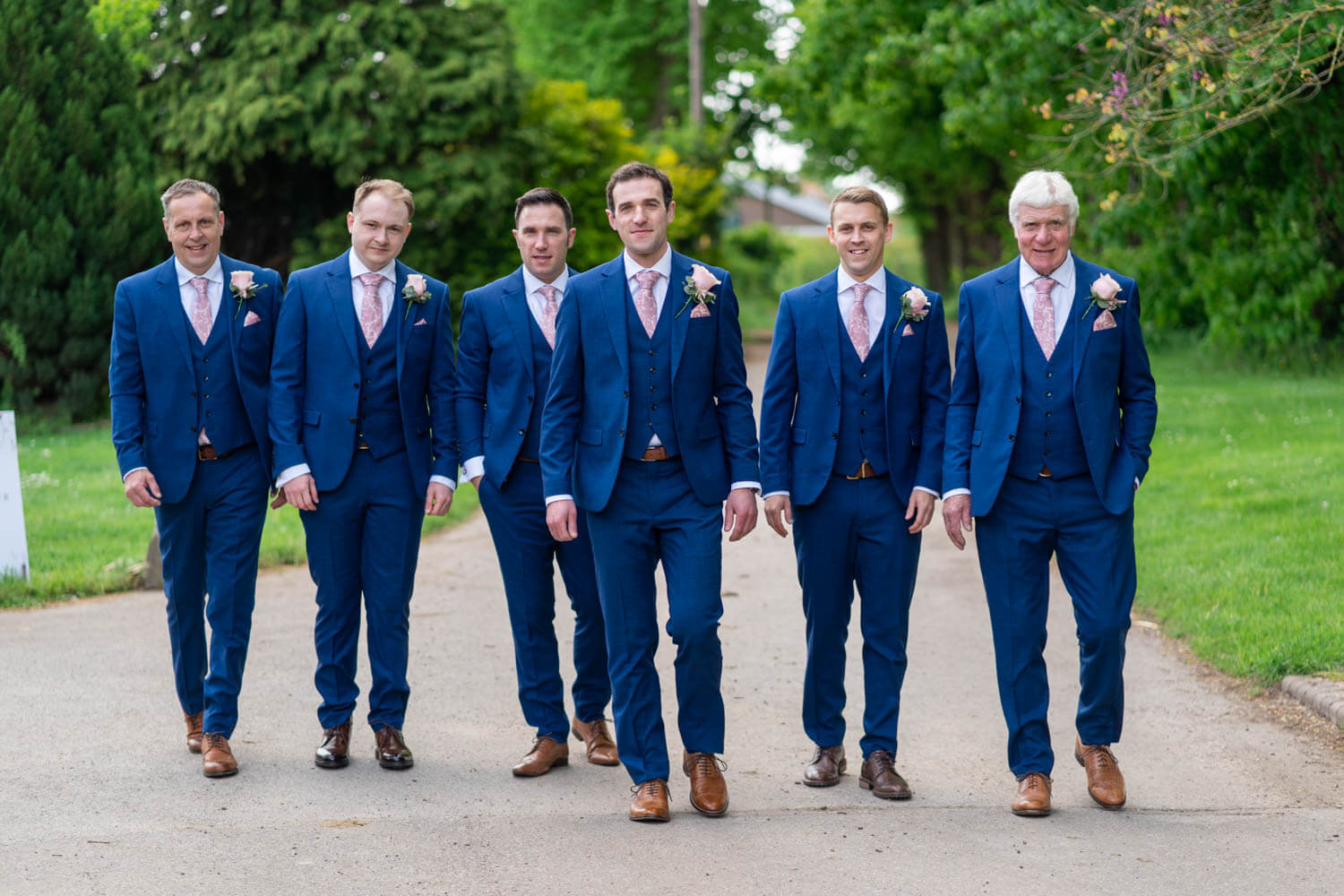 the groom and his groomsmen walk along the drive at Herons Farm