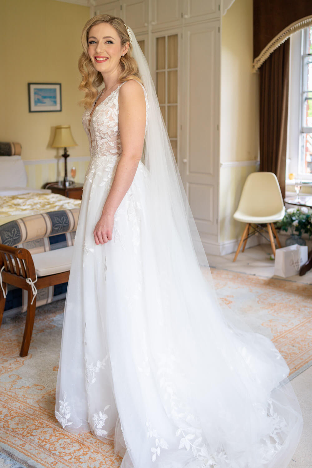the bride stands by the end of the bed in her beautiful dress before the ceremony at Herons Farm