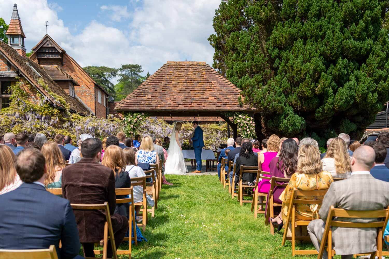 the wedding ceremony from the back, as the groom places the wedding ring on the bride's finger. They stand under the Pavilion at herons Farm