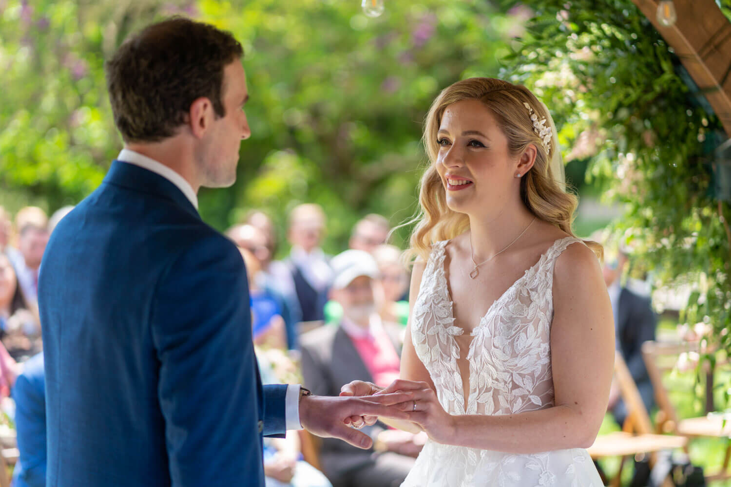 the bride looks at her groom as she places the wedding ring on his finger