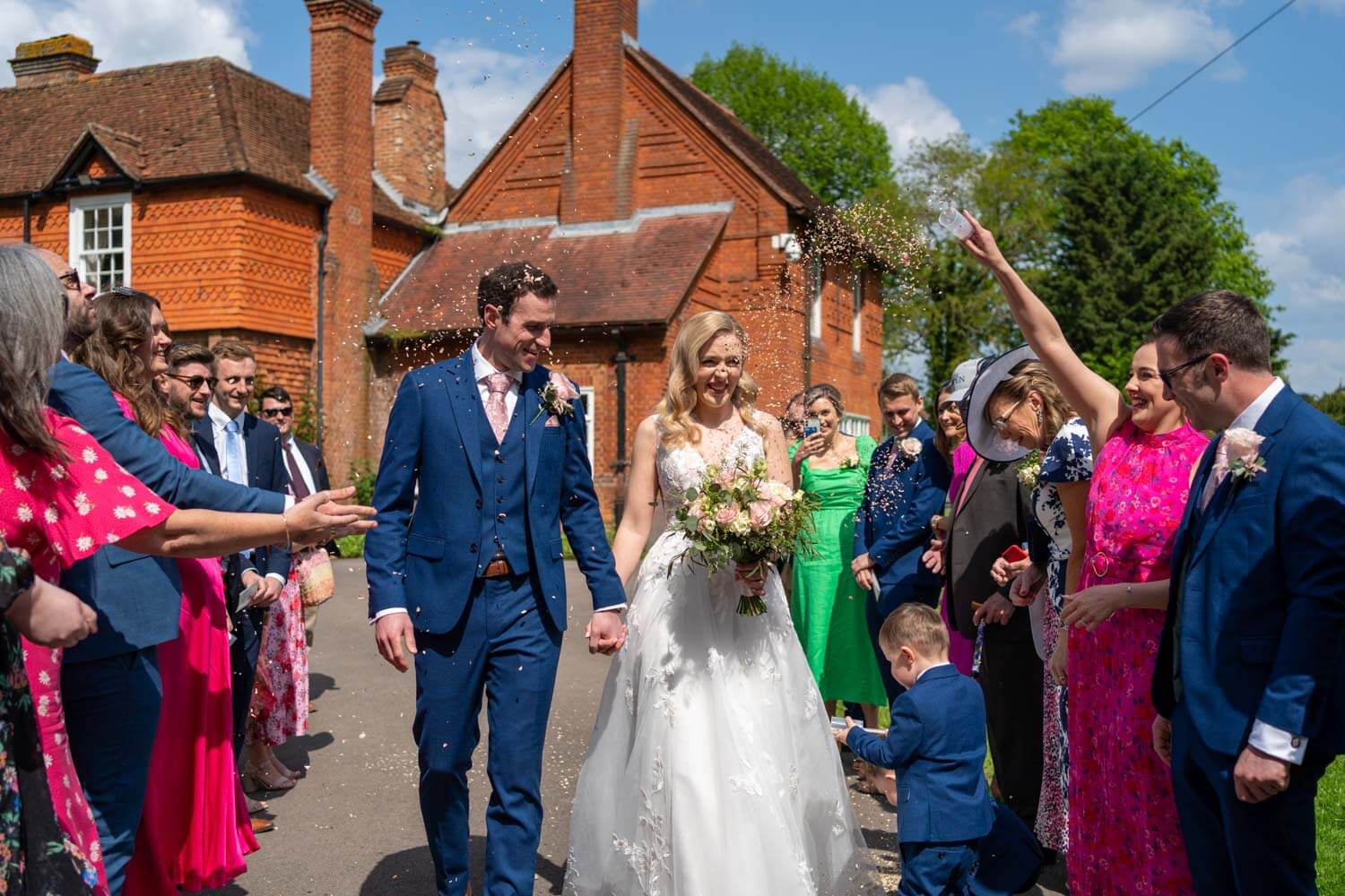 the wedding guests throw confetti as the bride and groom walk past, Herons Farm house is in the background