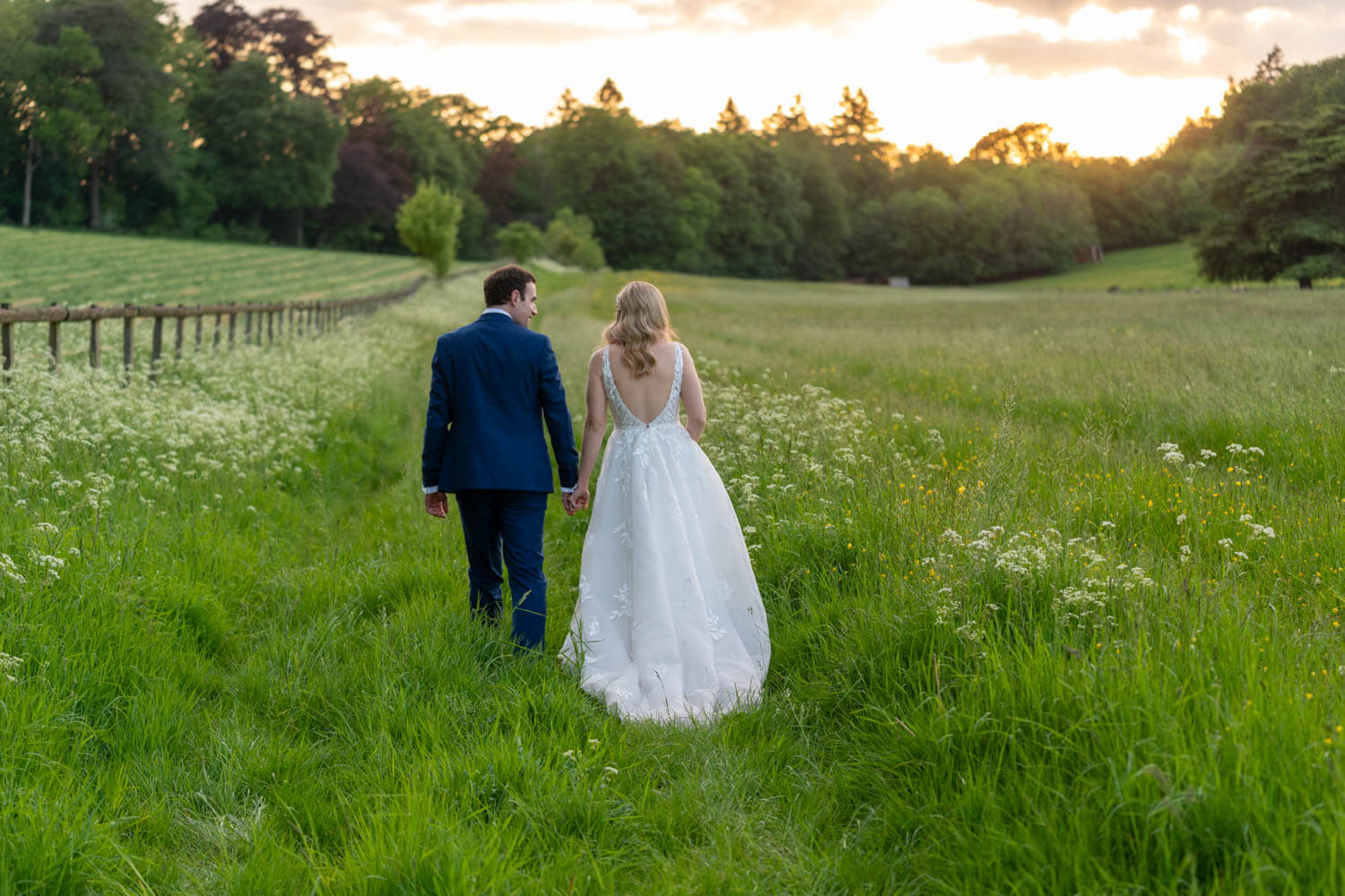 the bride and groom walk away throught the long grass at Herons Farm at sunset