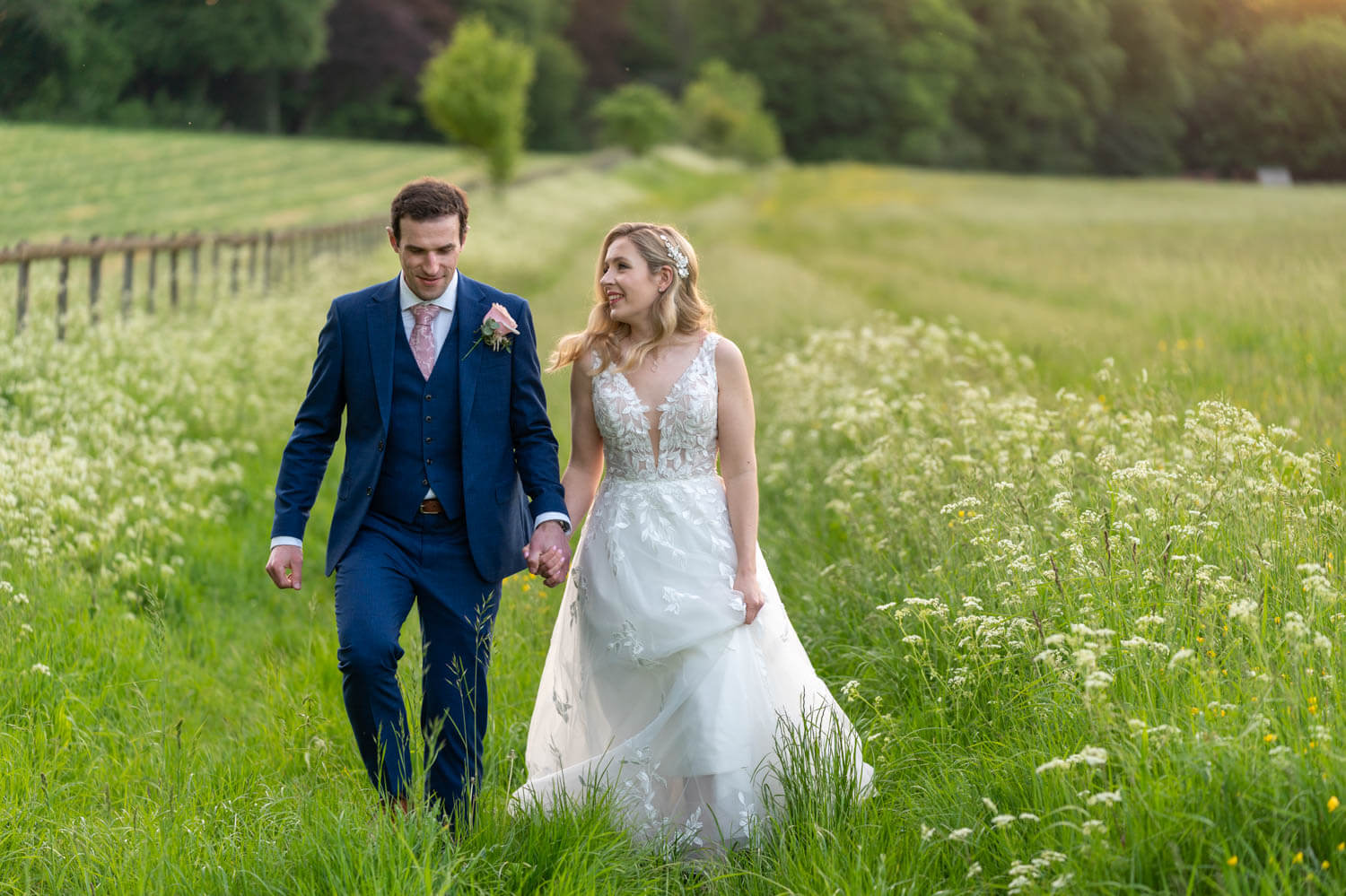 the bride and groom walk together and look at each other in the long grass and meadowsweet on the Gallops at Herons farm