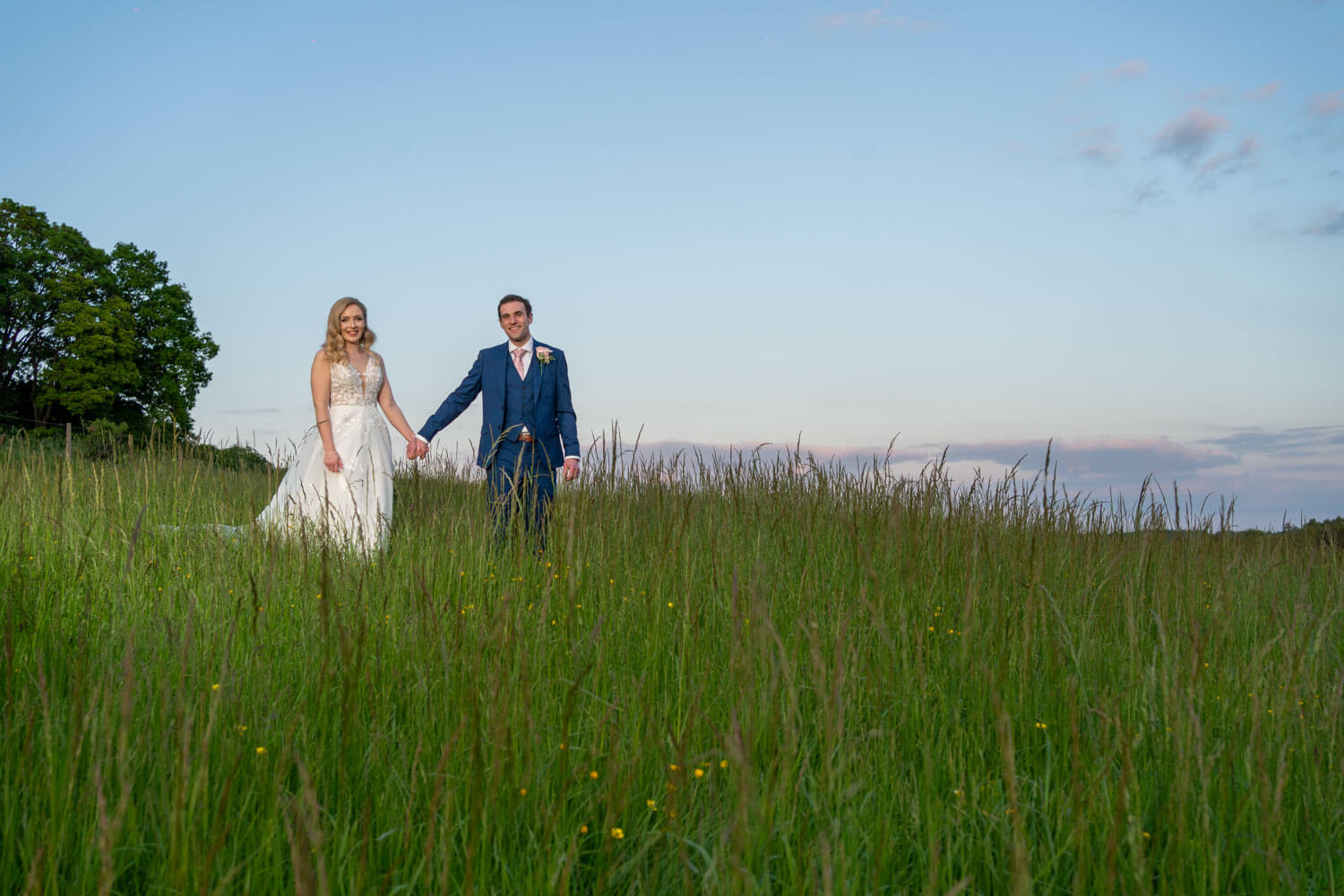 the bride and groom walk hand in hand at the Gallops at Herons Farm during golden hour