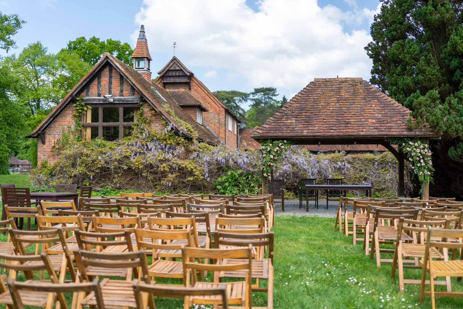 Chairs set out for the wedding ceremony under the pavilion, in the background we see the blooming wisteria