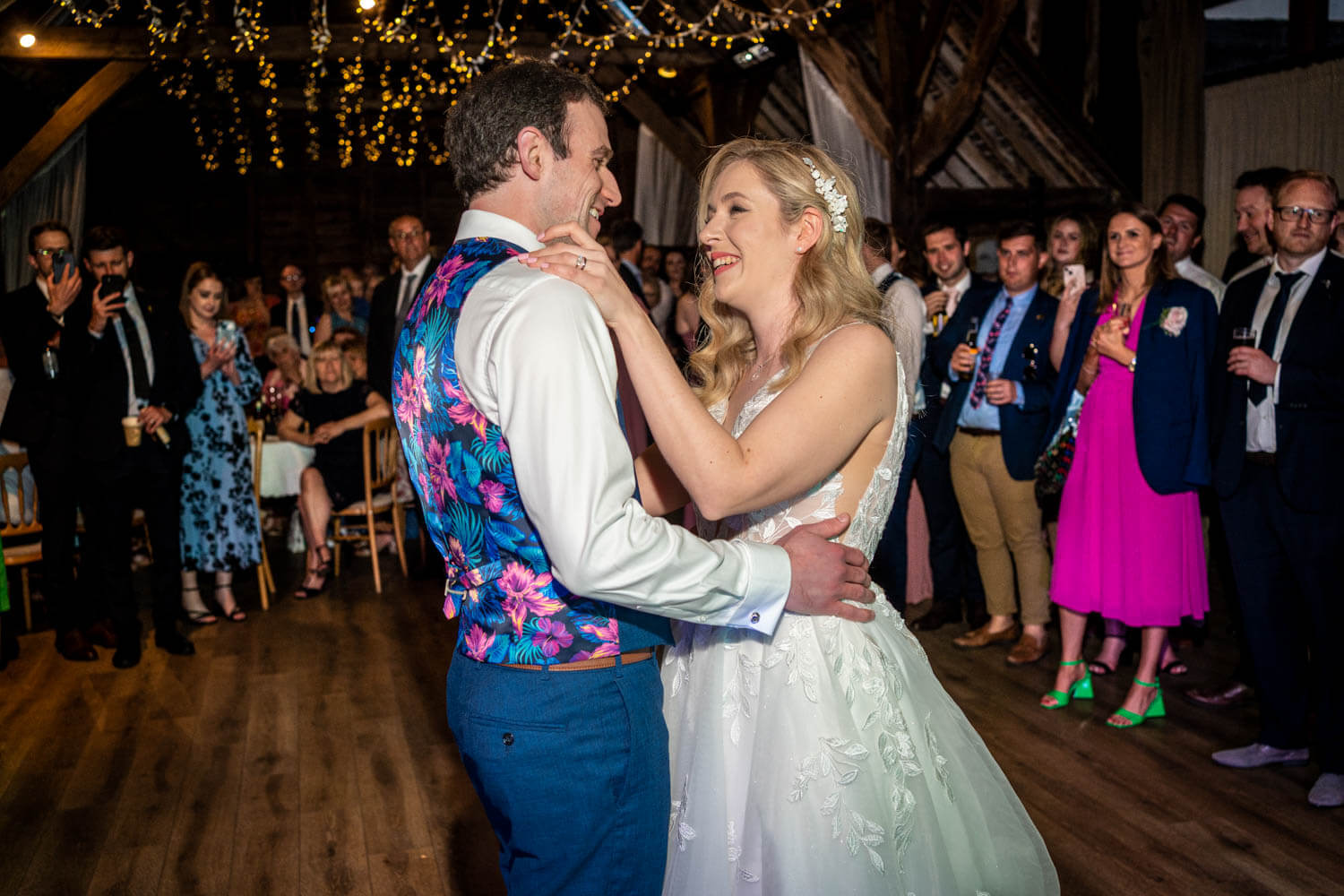 the smiling bride and groom enjoy their first dance in front of their wedding guests in the barn at Herons Farm
