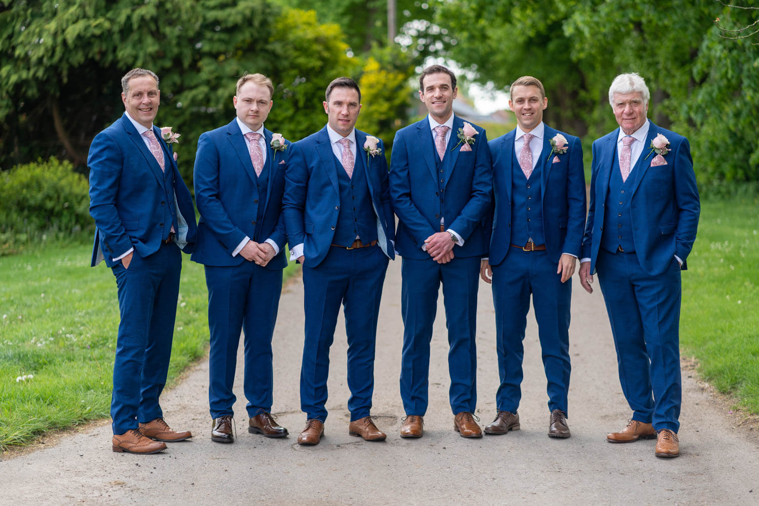 the groom and his groomsmen stand together on the drive at Herons Farm