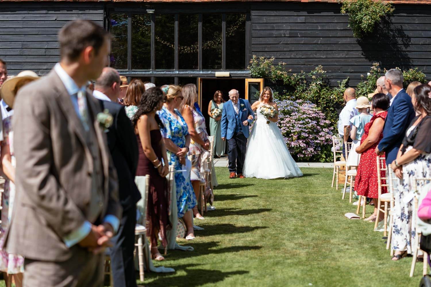 The bride walks down the aisle at Stokes Farm Barn on her father's arm.