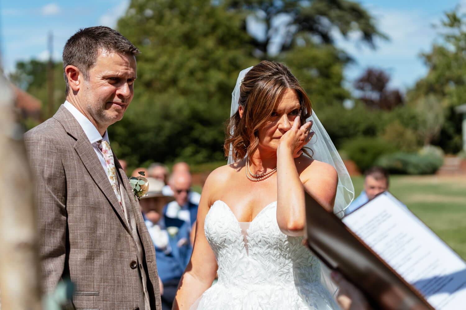 The bride wipes away a happy tear beside the groom during the vows.