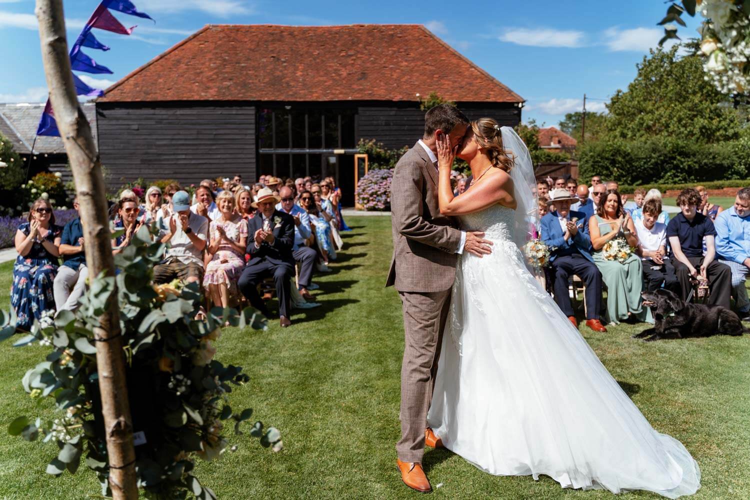 The bride and groom share their first kiss as newlyweds, Stokes Farm Barn in the background.