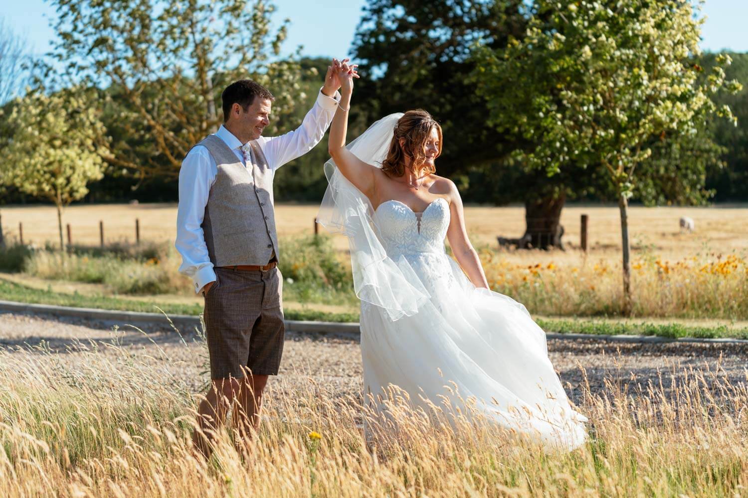 The groom twirls his bride across a sunlit field during their evening portraits at Stokes Farm Barn.