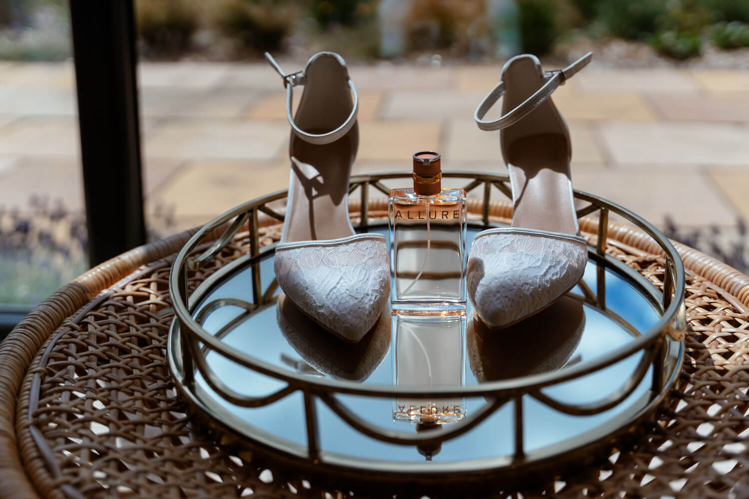 The bride's wedding shoes and perfume displayed on a mirrored tray.