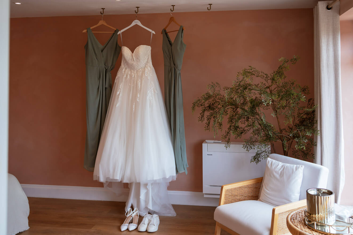 The wedding dress and bridesmaid dresses hang against a terracotta wall before the ceremony.